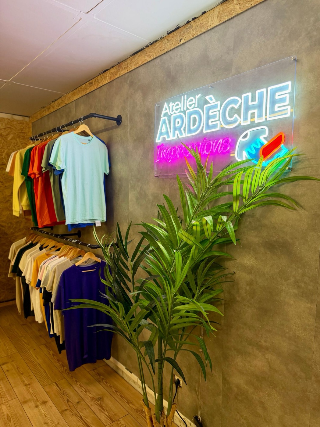 Le showroom de l'atelier : portants de t-shirts de couleur sous l'enseigne lumineuse